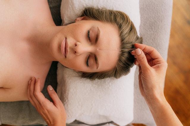a woman laying on a bed with a towel around her neck and receiving acupuncture treatment